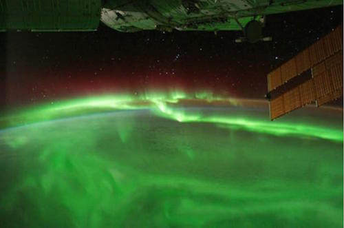 Aurora vista desde el espacio, que aparece como filamentos de gas con luz verde flotando sobre el planeta.